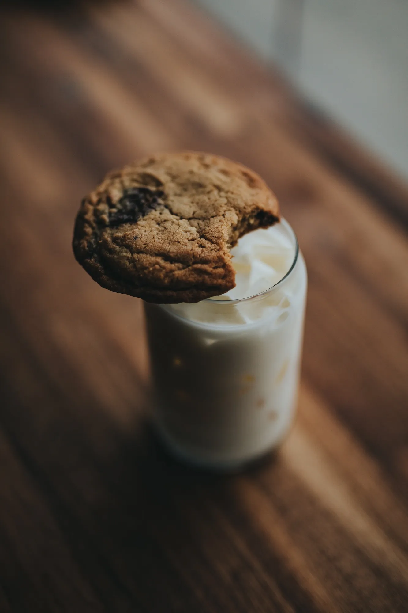 one chocolate chip cookie on top of a glass of milk on a wooden table