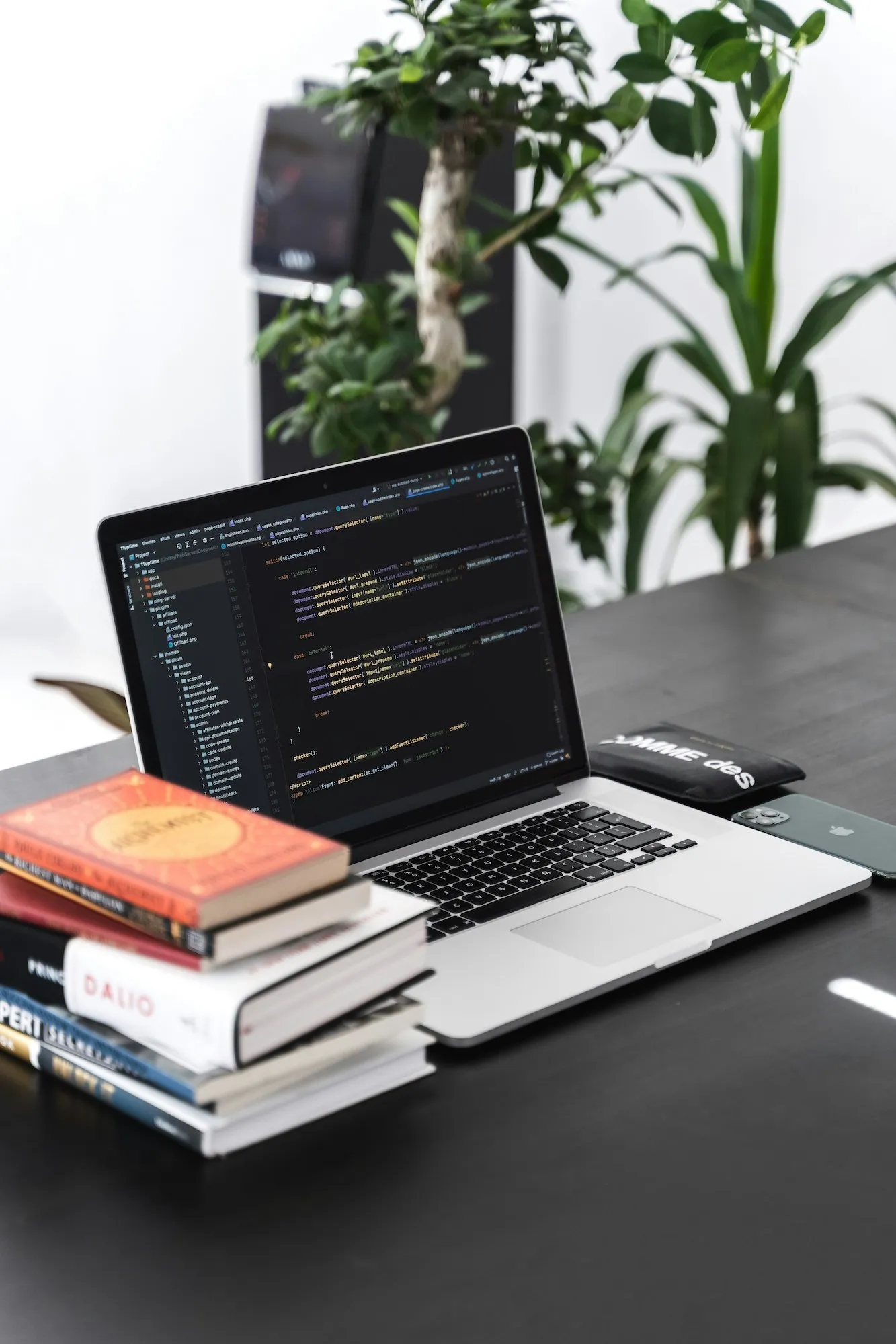 Macbook Pro on a black wooden table surrounded by books and a smartphone